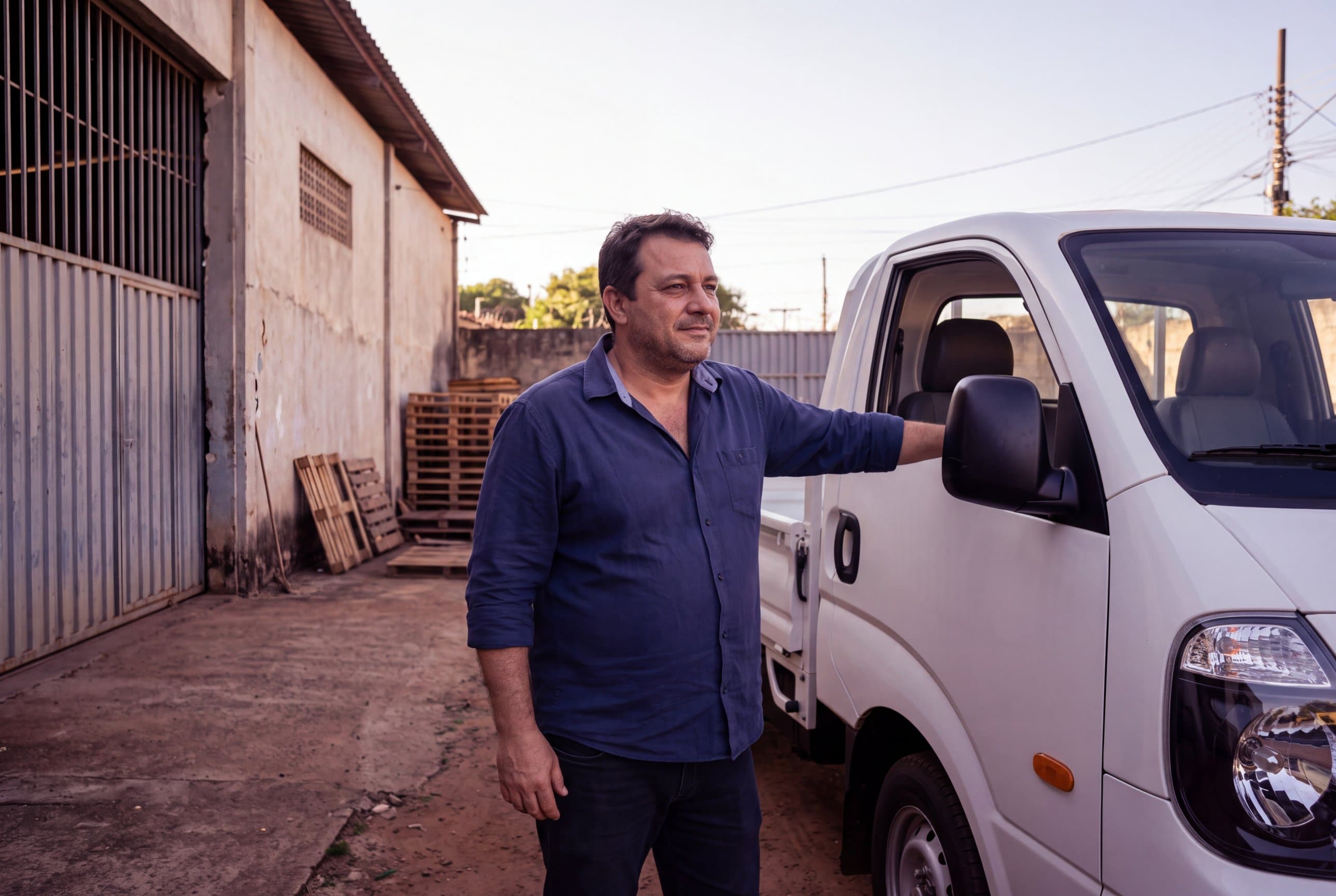 Empresário ao lado do caminhão novo, no pátio da empresa.