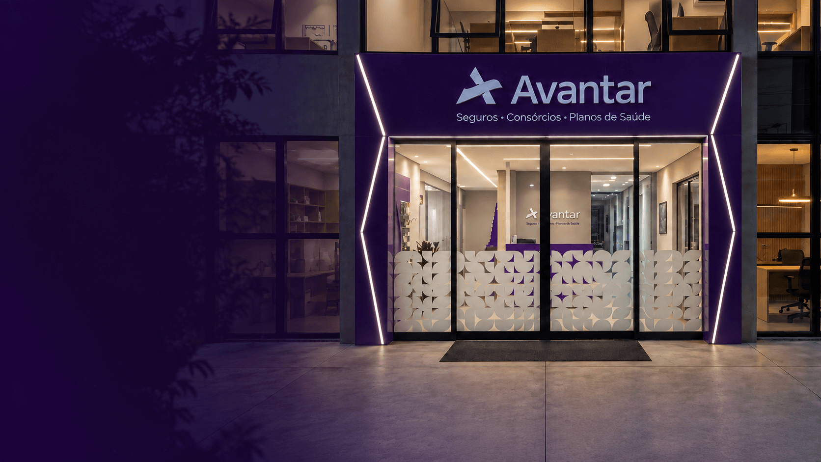 Fachada oficial de uma unidade Avantar, com o logotipo Avantar Seguros, Consórcios e Planos de Saúde iluminado à noite.